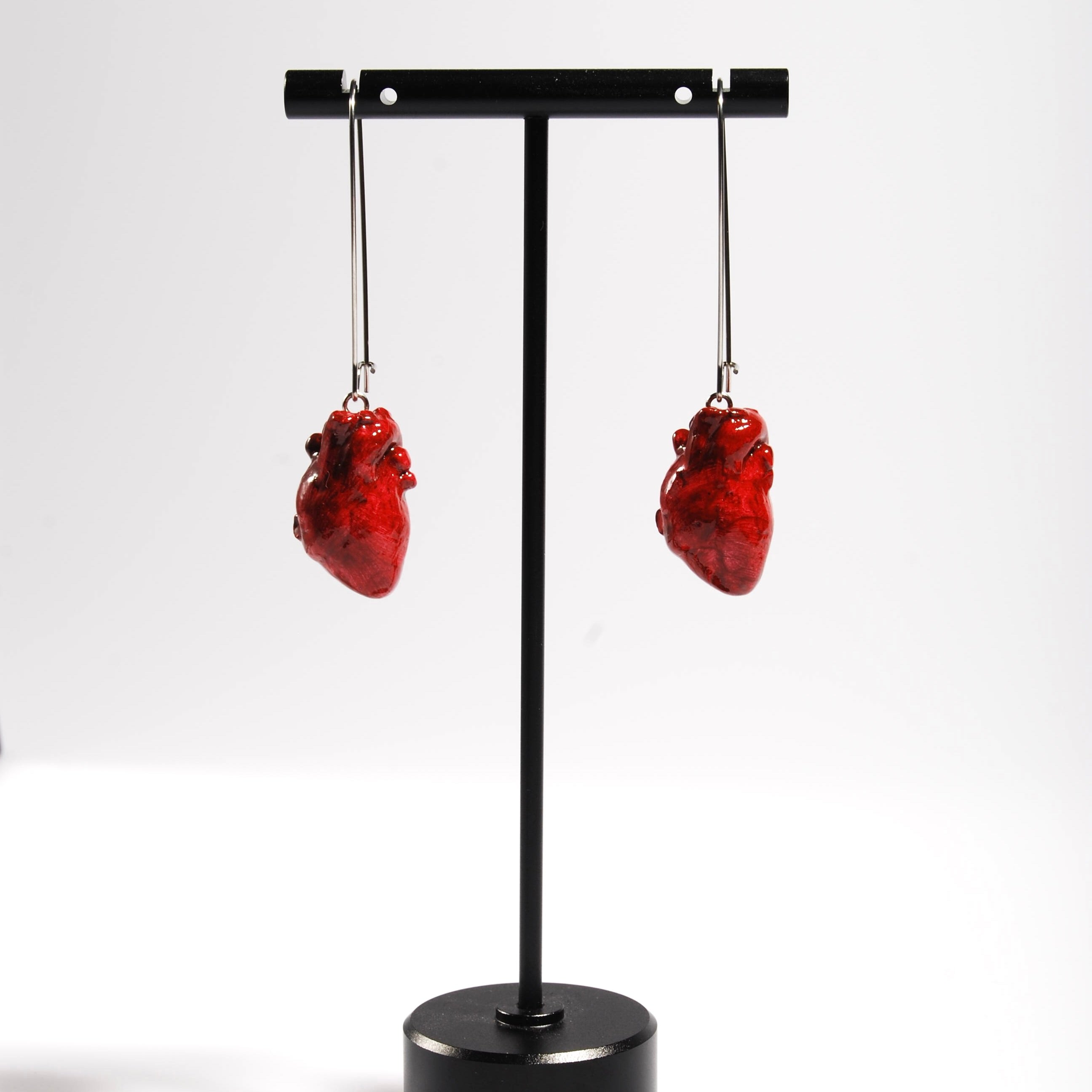 Orecchini cuore anatomico rosso con monachelle lunghe in acciaio appese su porta orecchini nero
