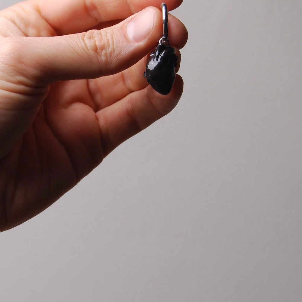 mano che tiene un orecchini a cerchio con cuore anatomico nero