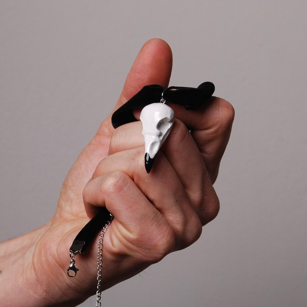 mano che impugna un choker run velluto nero con pendente miniatura di teschio di corvo