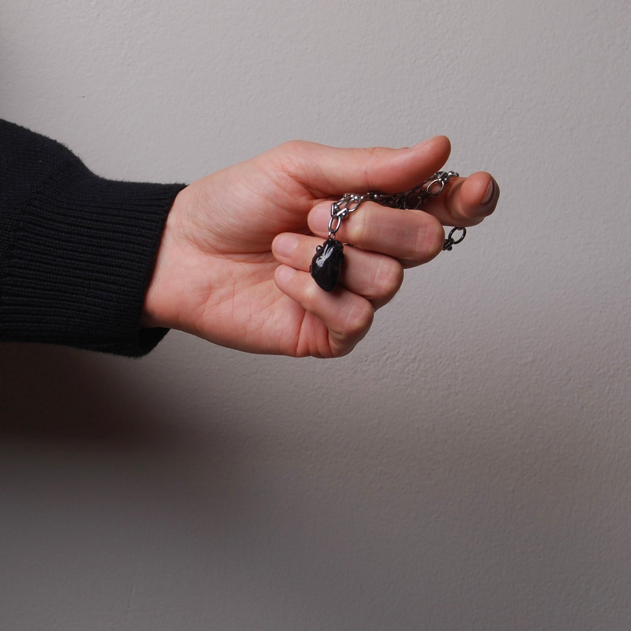 mano che tiene una collana catena spessa con pendente cuore anatomico nero