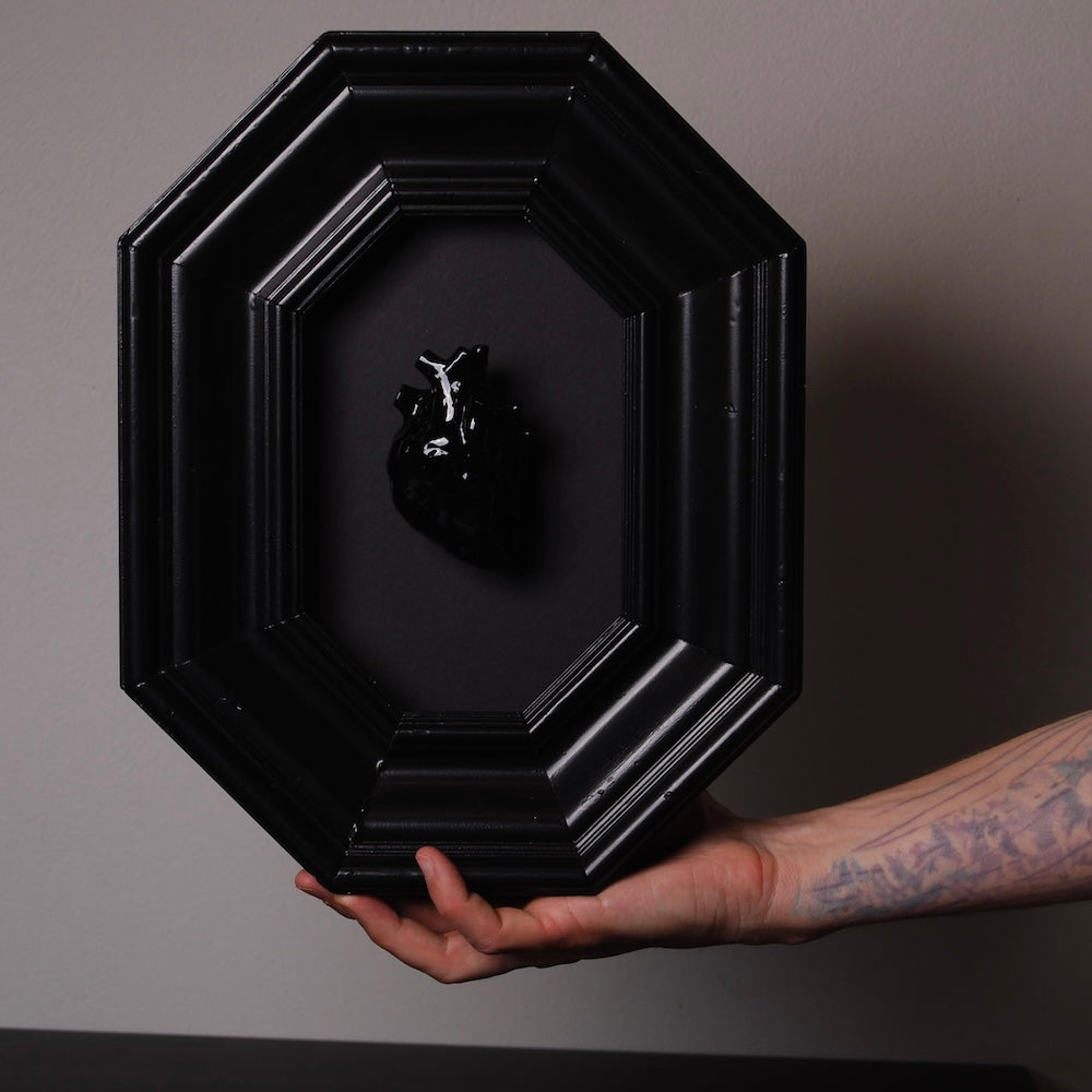 quadro con cornice ottagonale e cuore anatomico nero sorretto da una mano