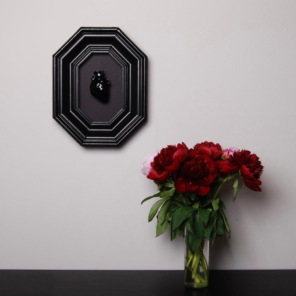 quadro con cornice ottagonale e cuore anatomico nero appeso in parete, sopra ad una scrivania con vaso con peonie