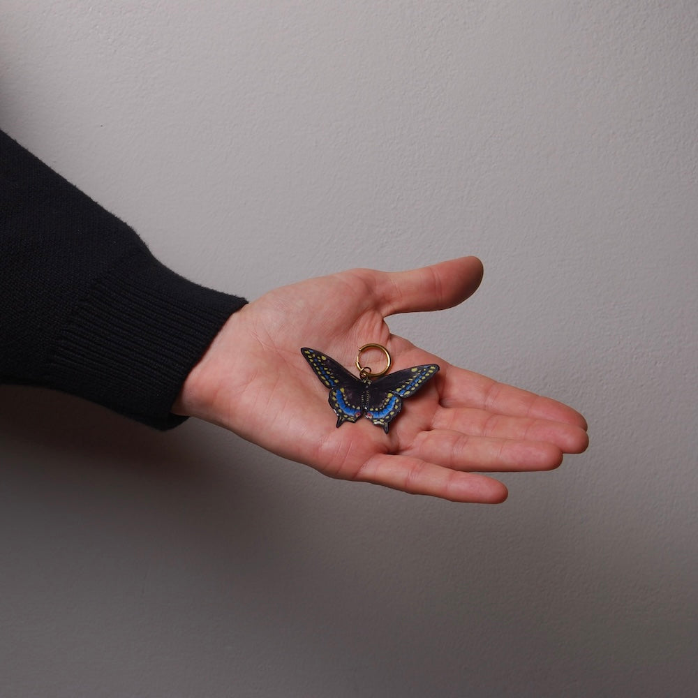 mano che tiene sul palmo un orecchino a cerchio con pendente farfalla nera