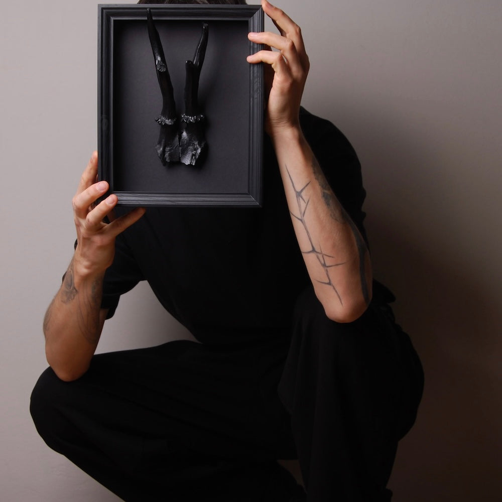 ragazzo accovacciato che sorregge un quadretto con riproduzione corna di capriolo