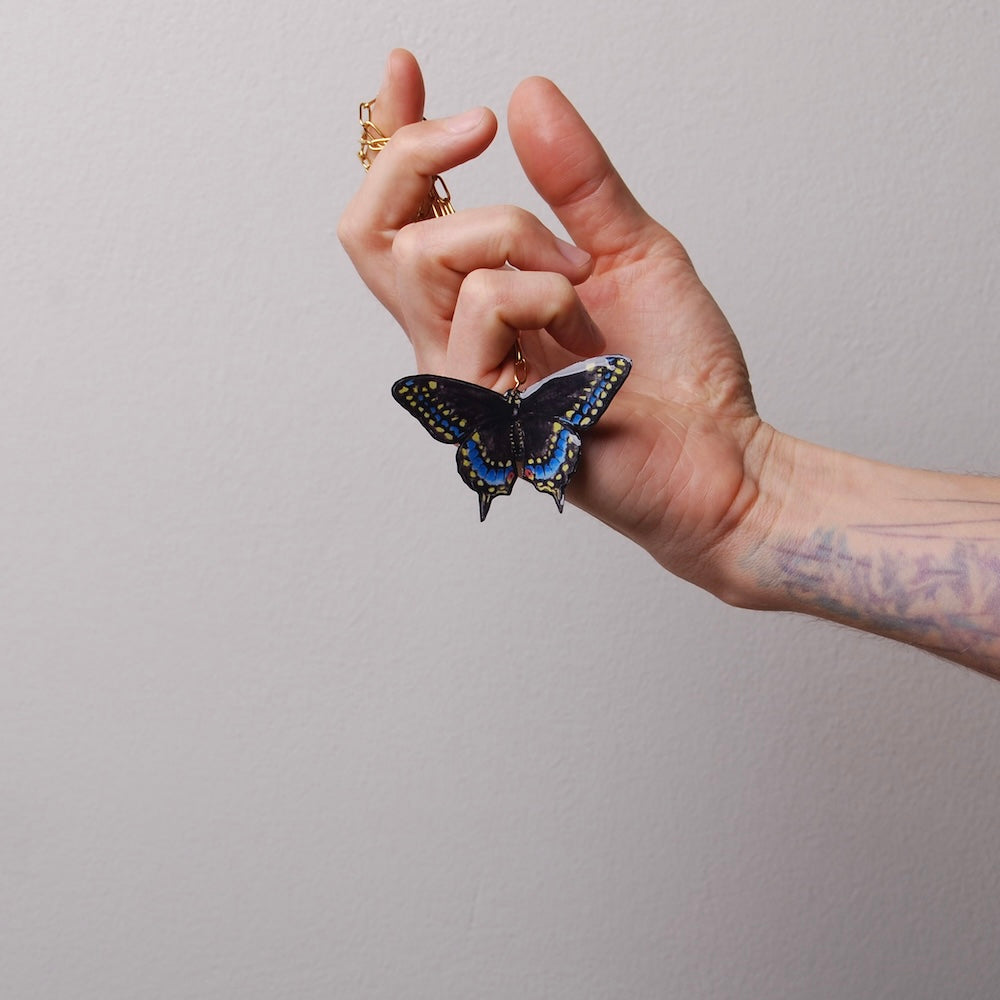 mano che tiene tra le dita una collana con farfalla nera
