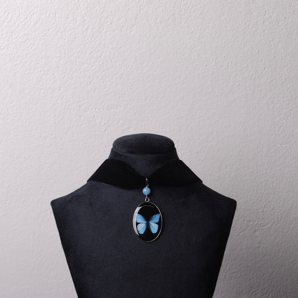 choker in velluto nero con pendente farfalla blu su espositore per collane nero
