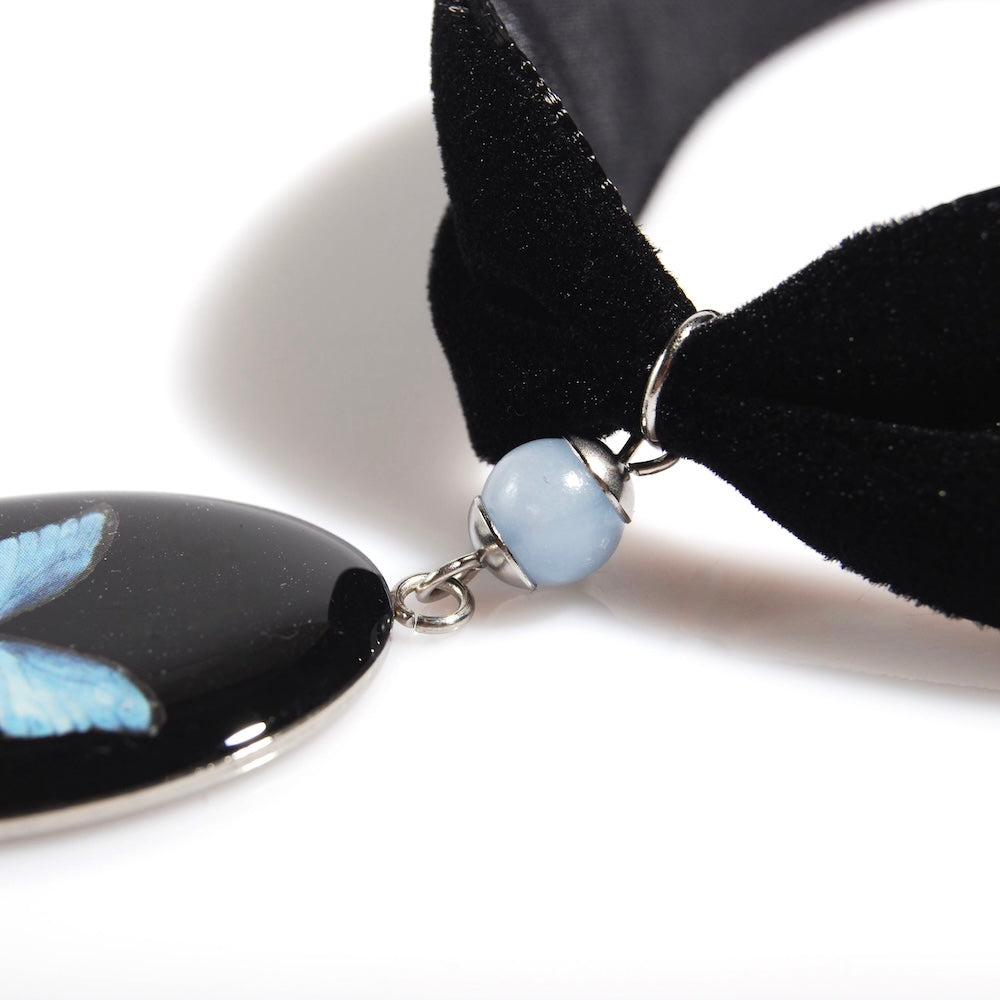 dettaglio della perla di celestina di un choker in velluto nero con pendente ovale e farfalla blu