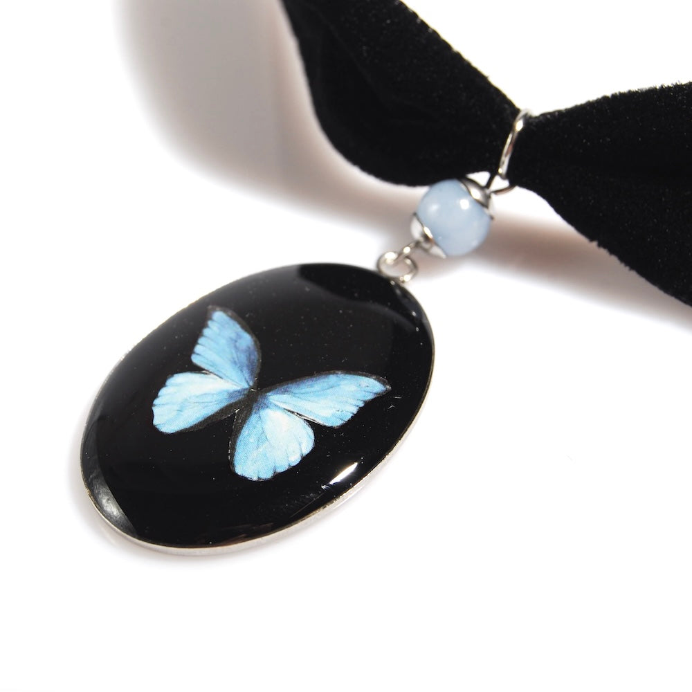 pendente ovale con farfalla blu appeso a un choker in velluto nero con dettaglio perla di celestina