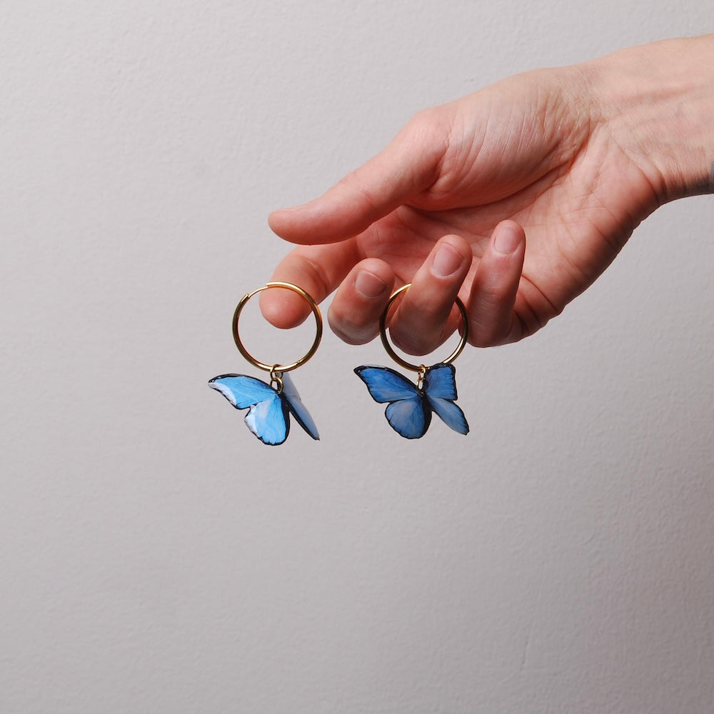 mano che tiene appesi alle dita orecchini a cerchio con farfalle blu