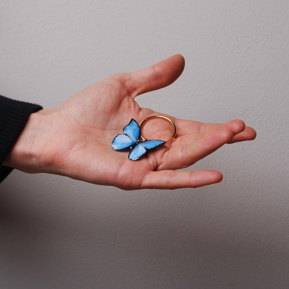 mano che tiene sul palmo un orecchino a cerchio con farfalla blu