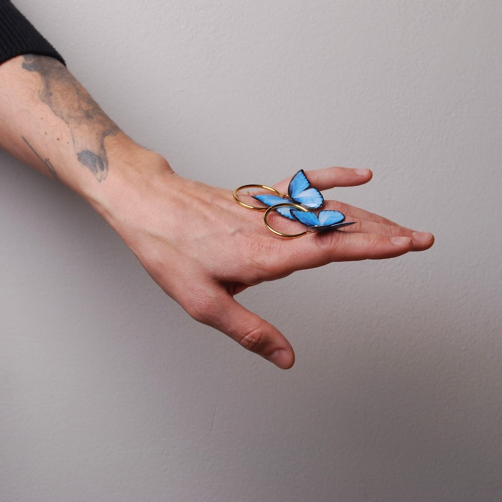 mano che tiene poggiati sul dorso orecchini a cerchio con farfalle blu