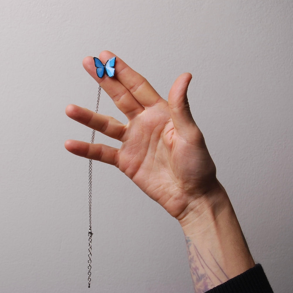 mano che tiene tra la dita una collana con farfalla blu