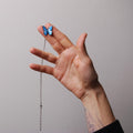 mano che tiene tra la dita una collana con farfalla blu