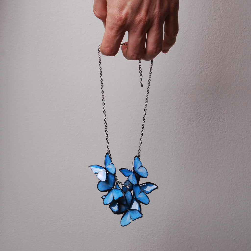 mano che tiene una collana con sciame di farfalle blu