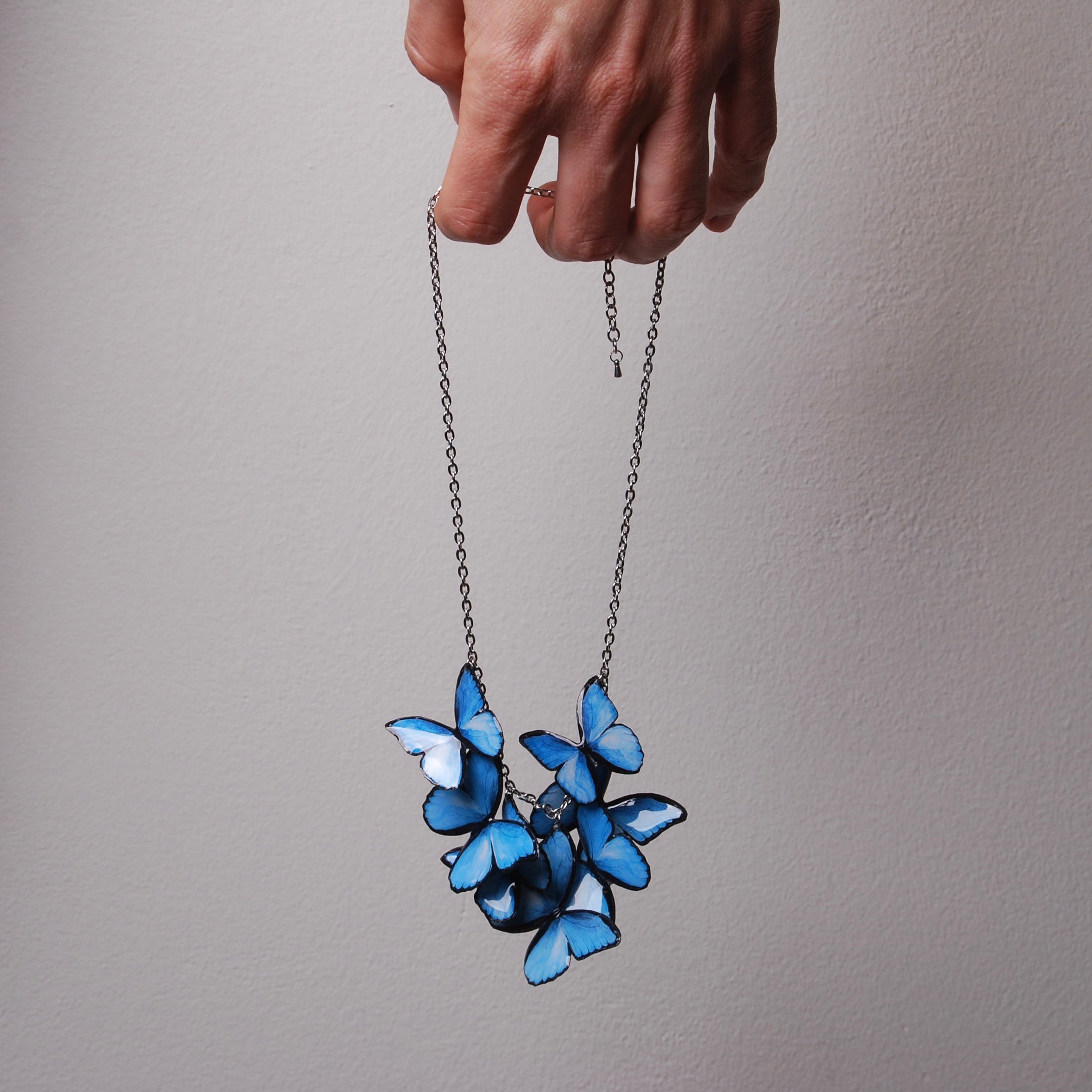 mano che tiene una collana con sciame di farfalle blu