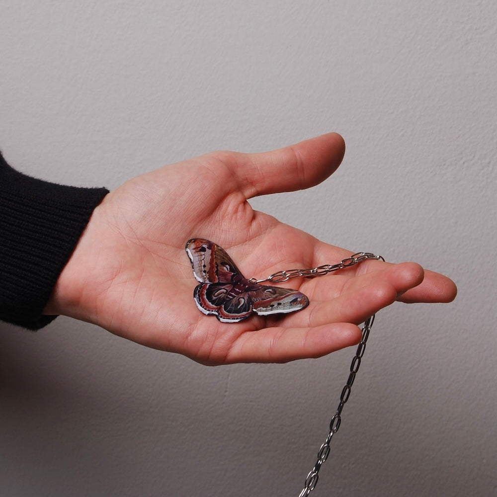 mano che tiene sul palmo una collana con pendente falena