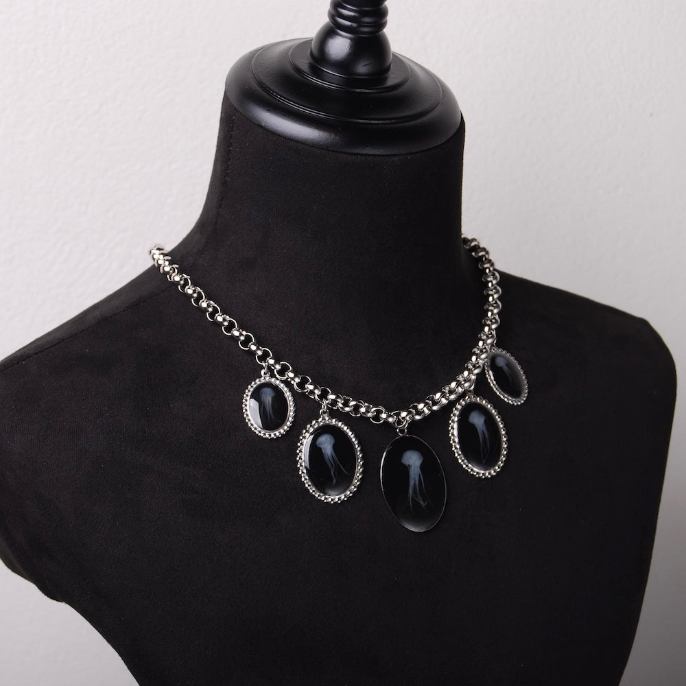 collana con 5 pendenti ovali con meduse marine inglobate sotto resina su busto espositore in velluto nero, vista 3/4