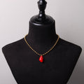 collana con catena a sfere in acciaio placcato oro e pendente cuore anatomico rosso in resina minerale, su busto espositore in velluto nero