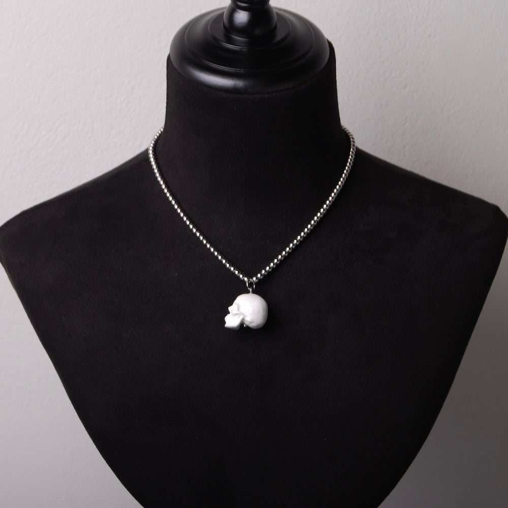 collana catena e sfere in acciaio con pendente teschio bianco in resina minerale, su busto espositore in velluto nero