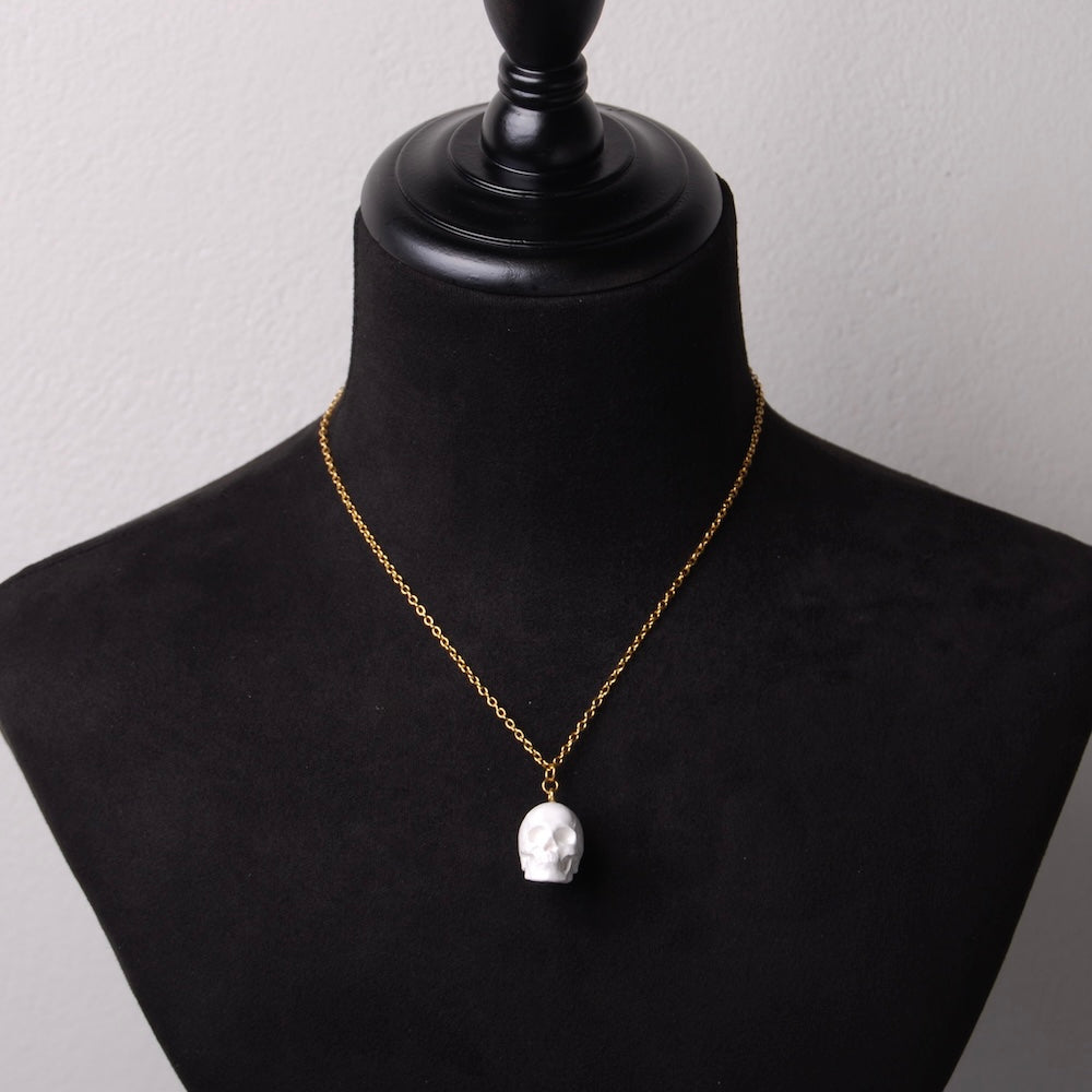 collana a catena sottile in acciaio placcato oro con pendente teschio bianco in resina minerale, su busto espositore in velluto nero