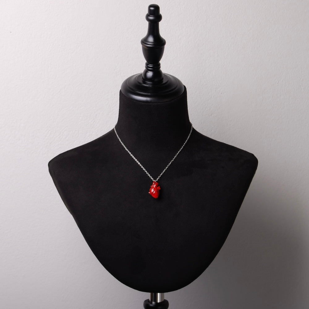 collana con catena sottile in acciaio e pendente cuore anatomico rosso in resina minerale, su busto espositore in velluto nero