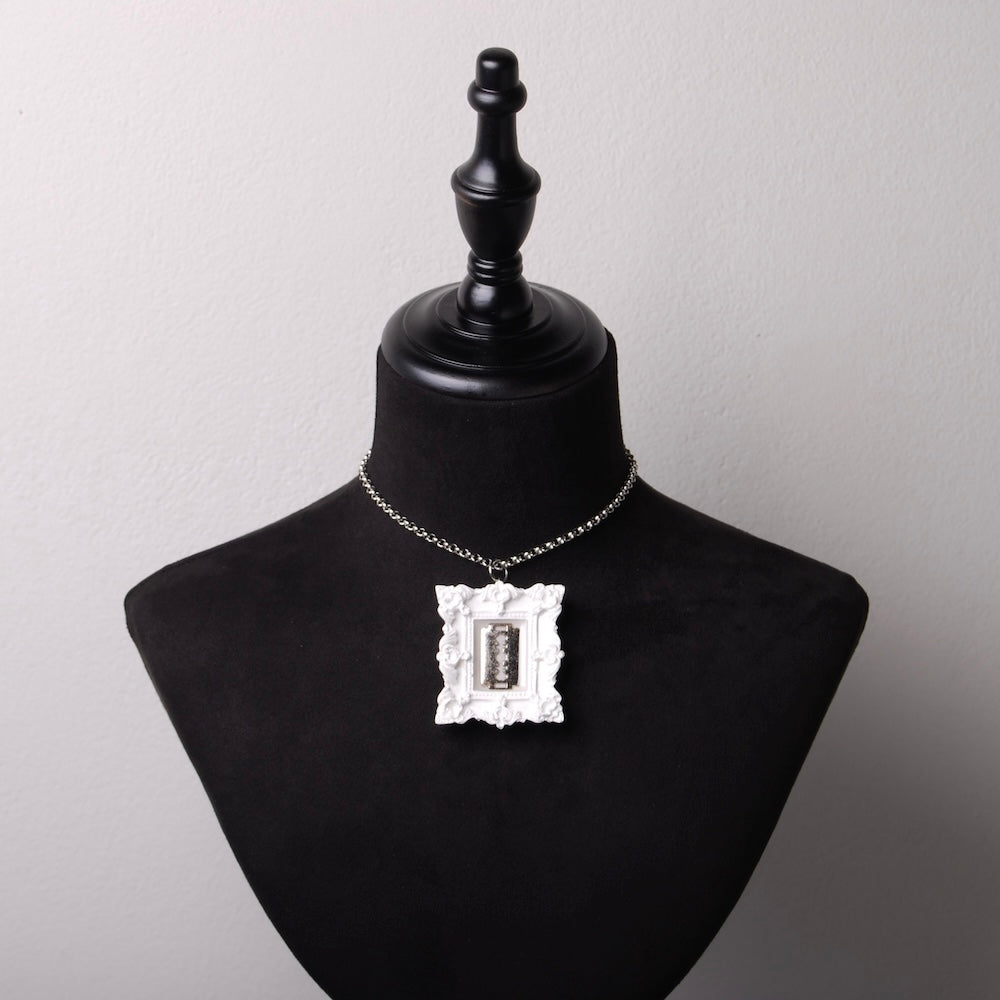 girocollo con catena in acciaio e pendente cornice barocca con lametta, su busto espositore in velluto nero