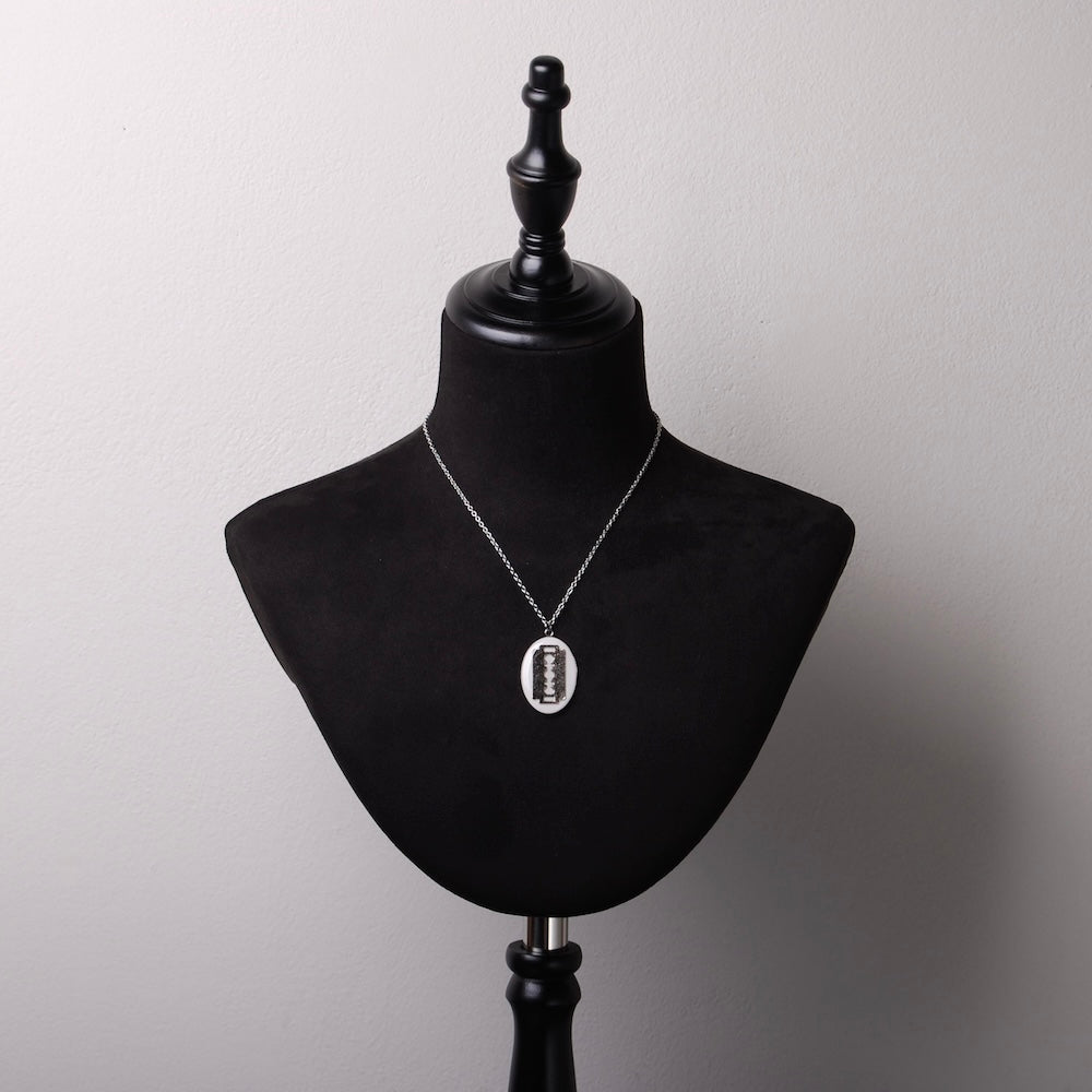 collana pendente ovale con lametta inglobata sotto resina su busto espositore in velluto nero