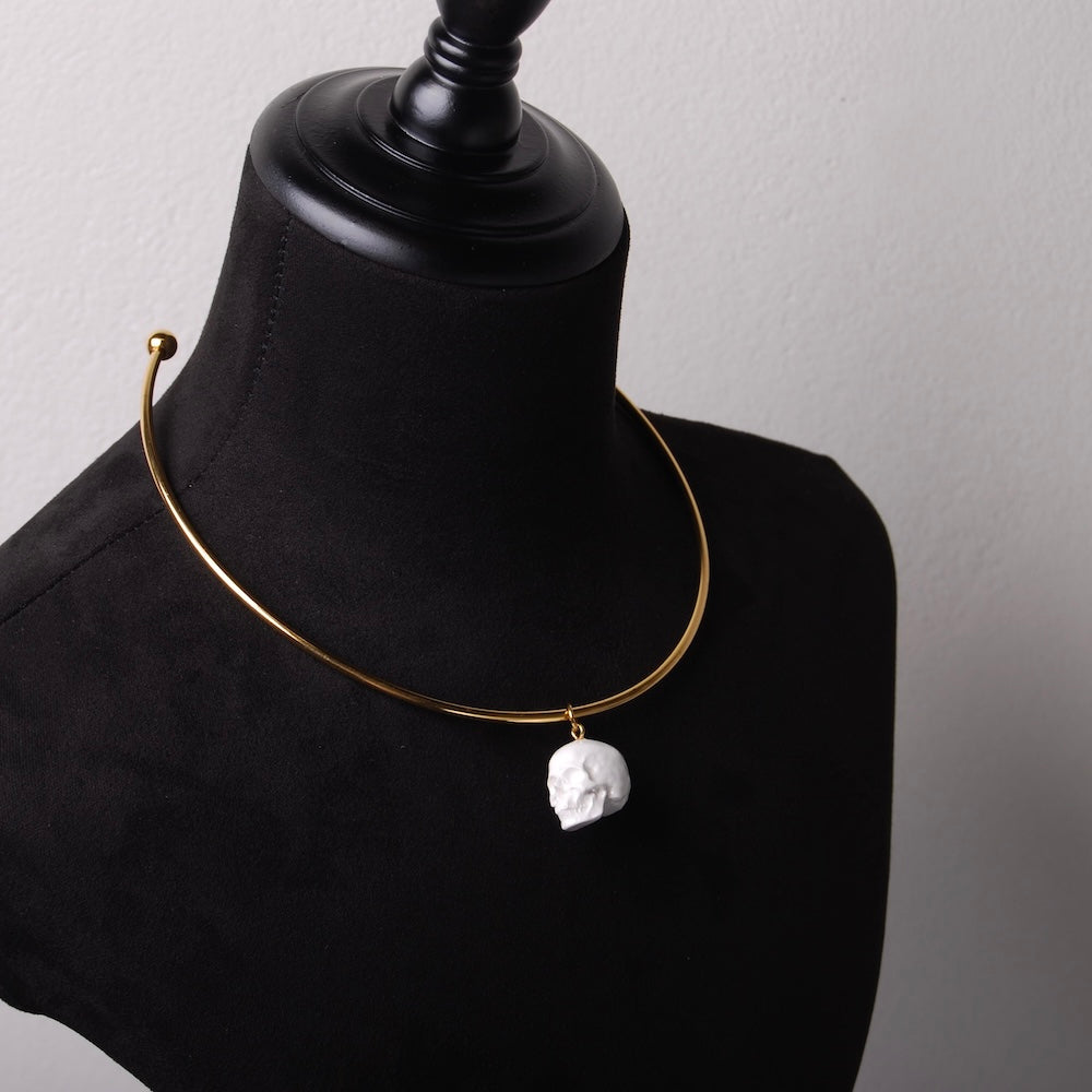 girocollo rigido in acciaio inox placcato oro con pendente teschio bianco in resina minerale, su busto espositore in velluto nero