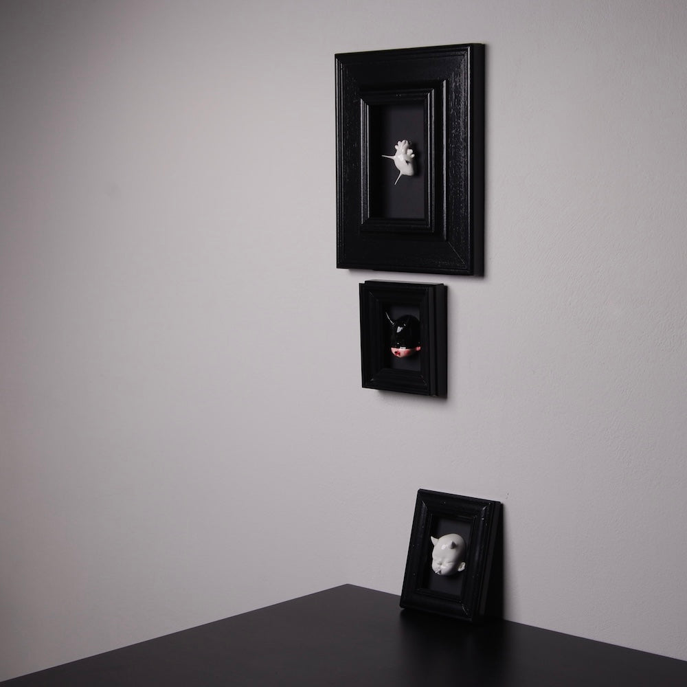 tre quadretti con miniature cuori e teste di bambole appesi al muro e appoggiati su una scrivania