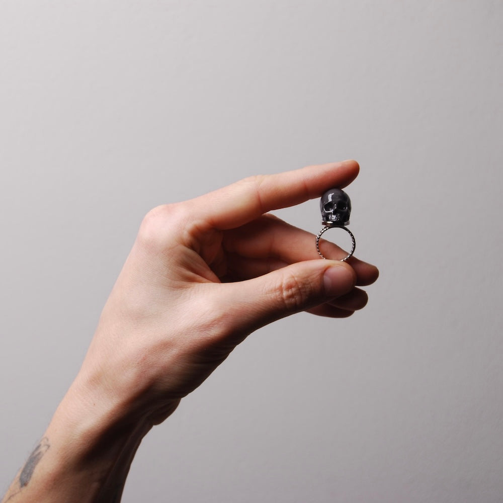 mano che tiene tra le dita un anello con teschio grigio scuro