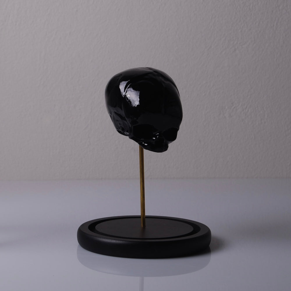 piccolo teschio nero su piedistallo sottile e base in legno