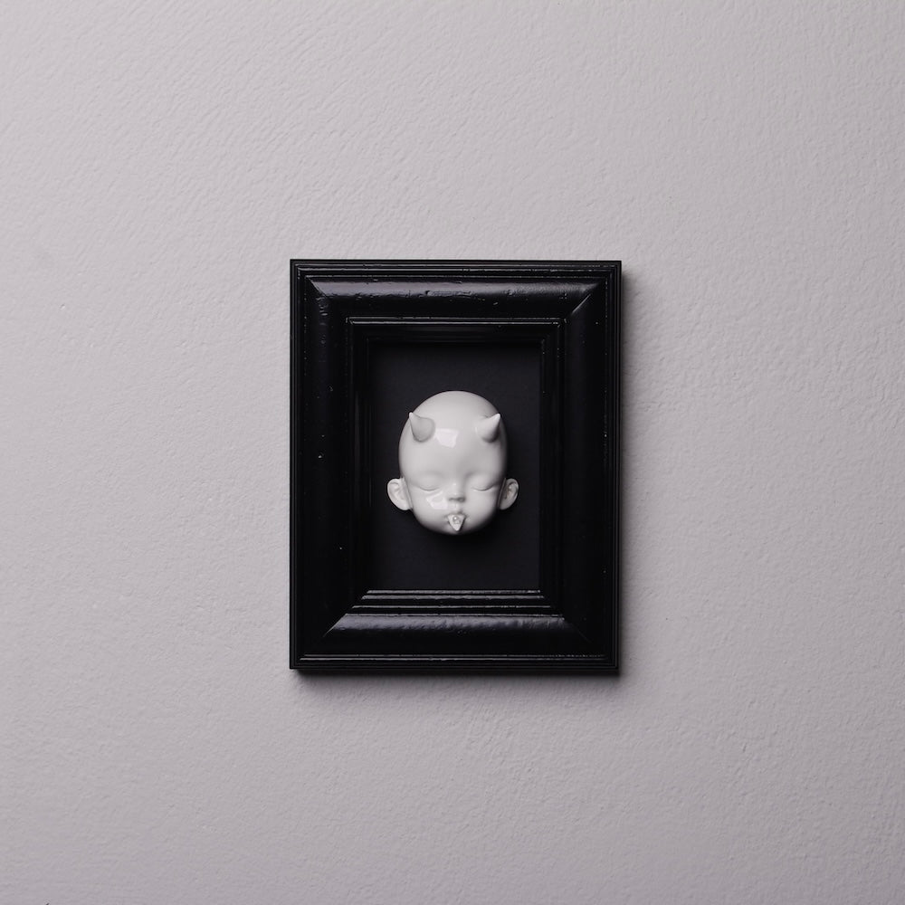 testa di bambola bianca con corna dentro ad un quadretto nero