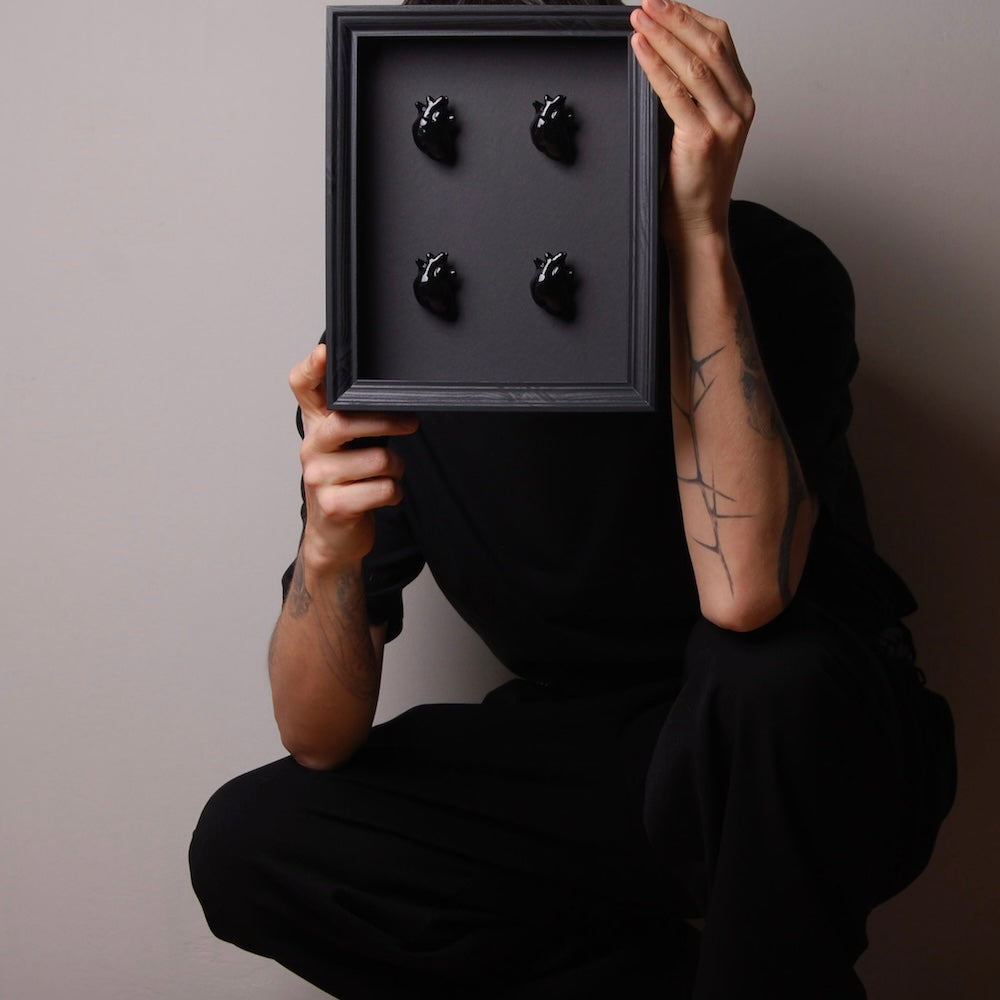 ragazzo accovacciato che tiene tra le mani un quadretto con 4 miniature di cuore anatomico nero