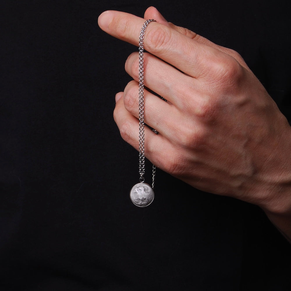 mano che tiene una collana con pendente cabochon con luna piena 