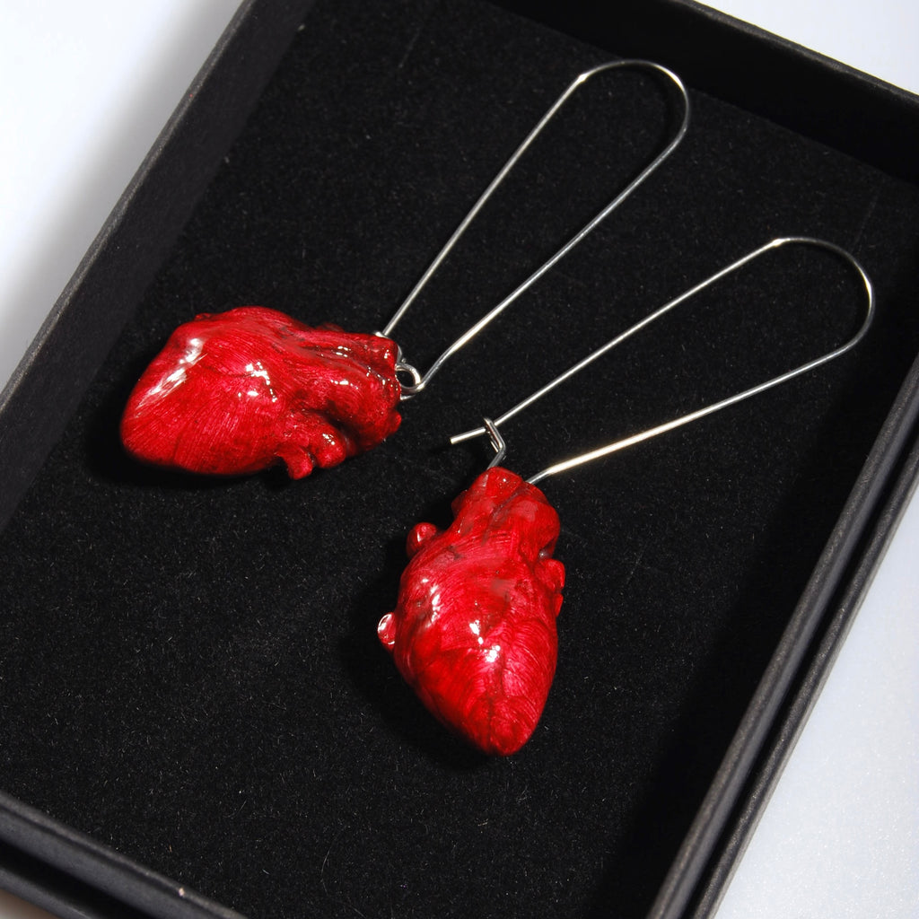Dettaglio orecchini con cuore anatomico rosso e monachelle lunghe in acciaio dentro scatolina nera