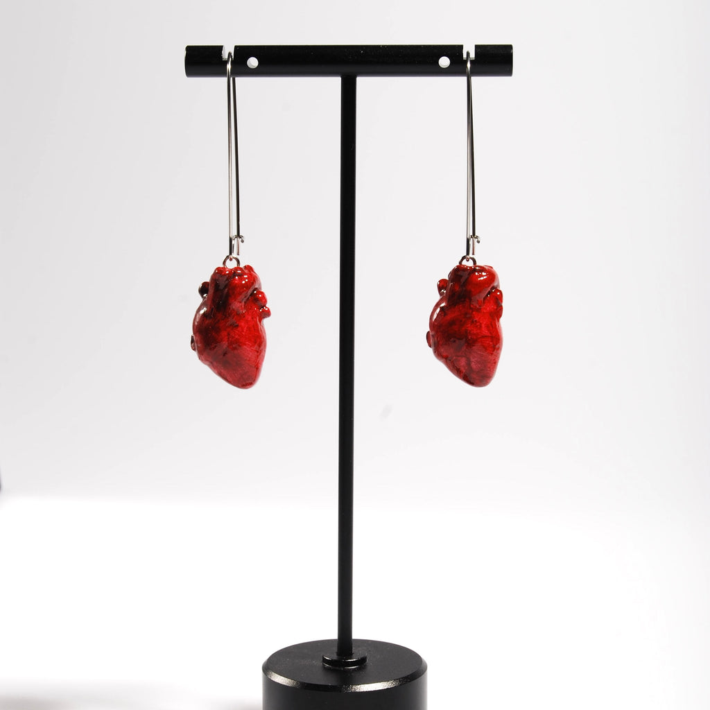Orecchini cuore anatomico rosso con monachelle lunghe in acciaio appese su porta orecchini nero