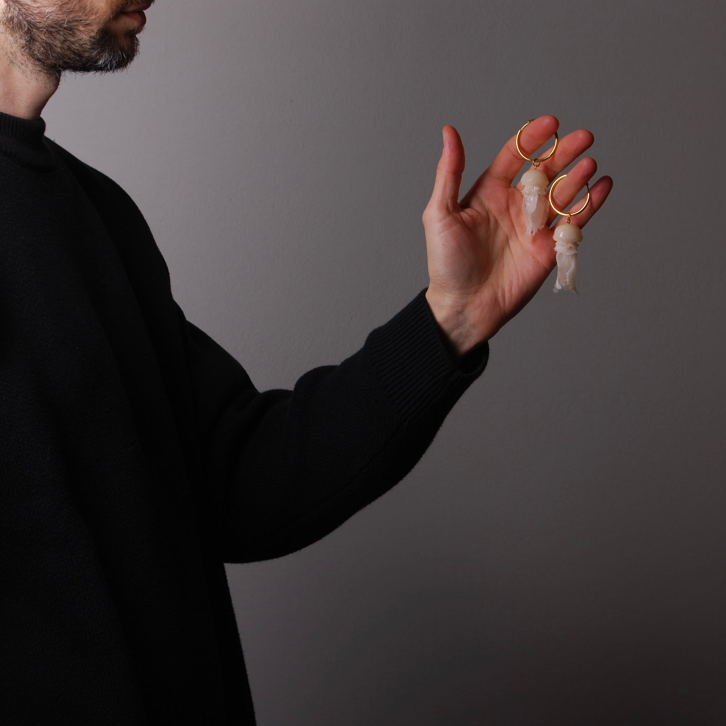 mano che tiene un paio di orecchini a cerchio grande con pendente medusa marina