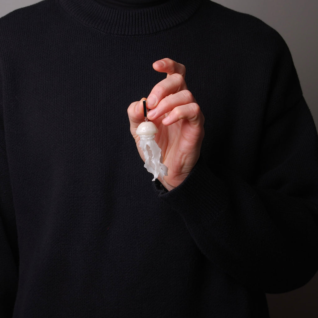 mano che sorregge un orecchino con perno rettangolare con pendente medusa marina