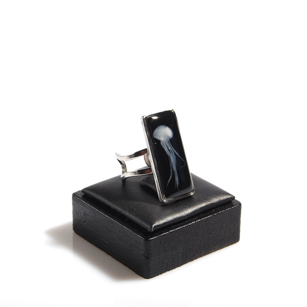 anello rettangolare con medusa sotto resina poggiato su porta anelli in legno