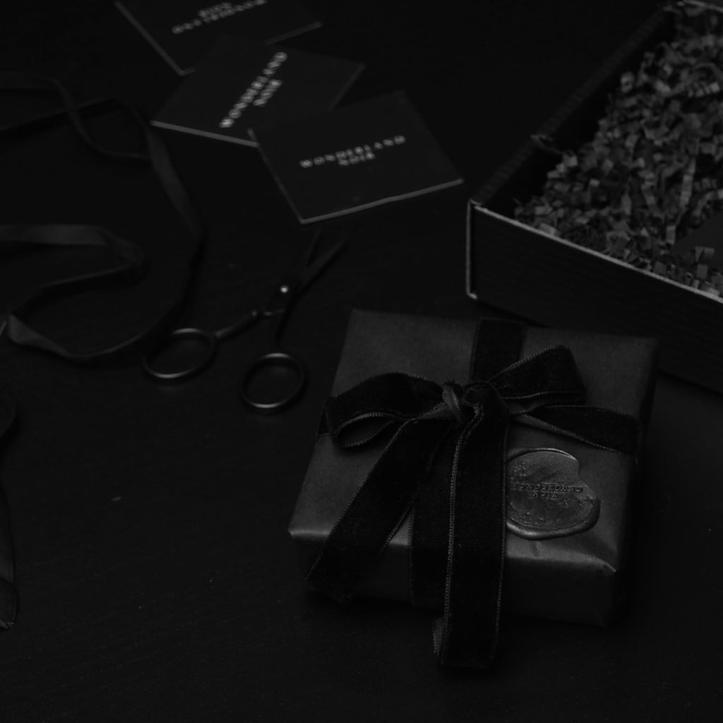 scatola regalo nera con nastro in velluto nero, poggiata su ripiano nero con forbici e materiale da imballaggio nero