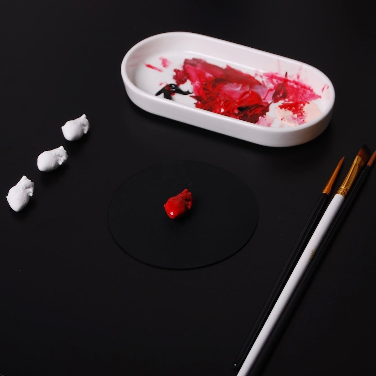 piccolo ciondolo a forma di cuore anatomico rosso poggiato su un tavolo, con altri cuori bianchi a lato e pennelli e colori