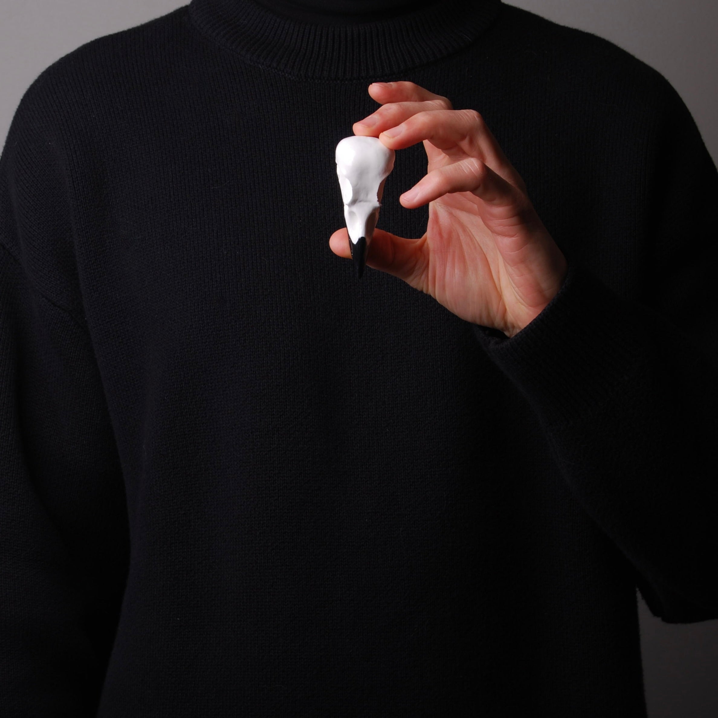 mano che tiene una spilla a forma di teschio di corvo bianco con punta del becco nero
