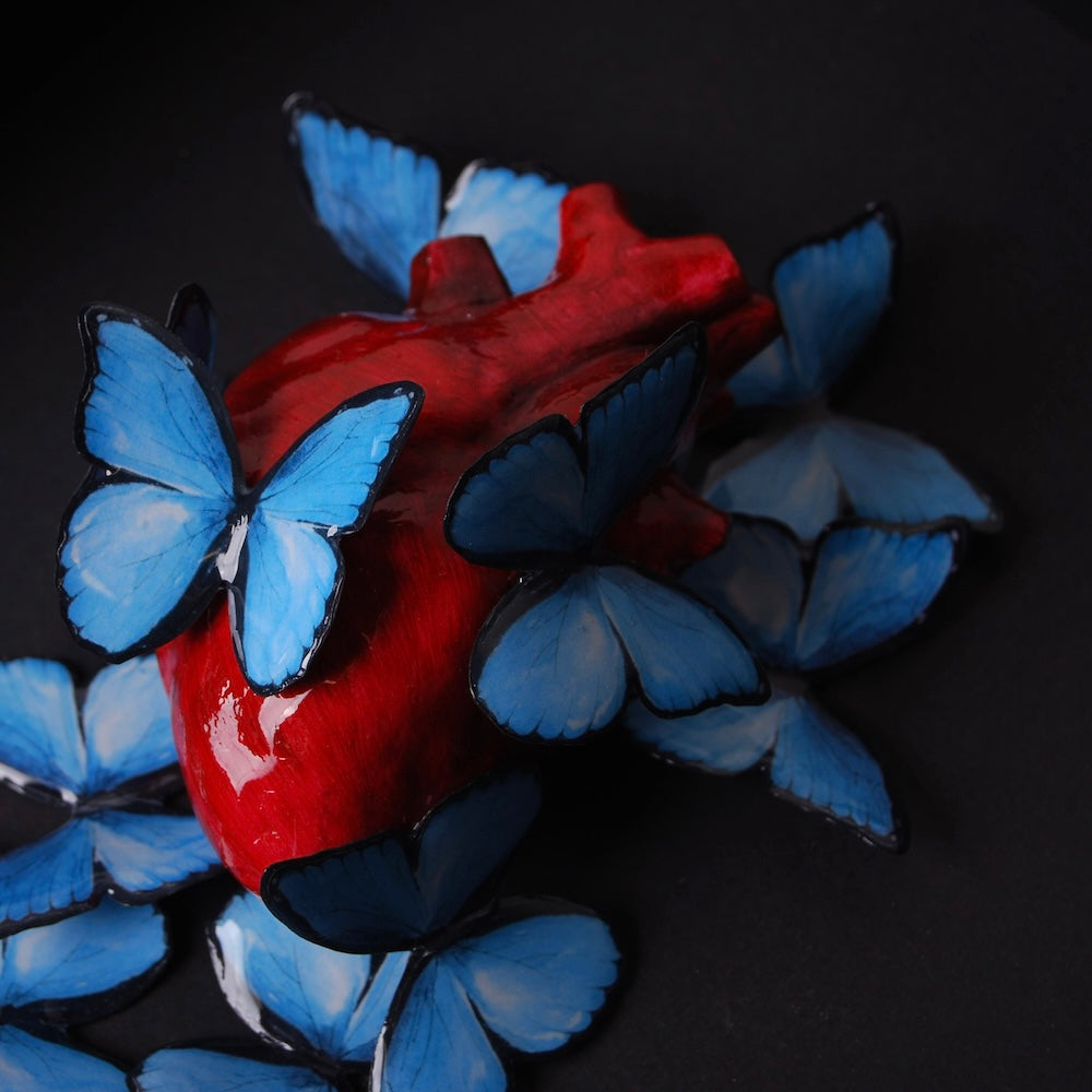 cuore anatomico rosso circondato da farfalle blu