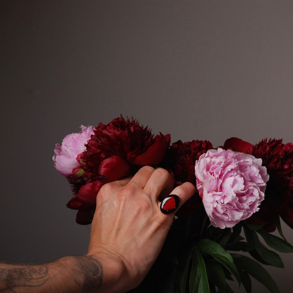 anello con cammeo cuore anatomico indossato da mano maschile che tocca peonie in vaso