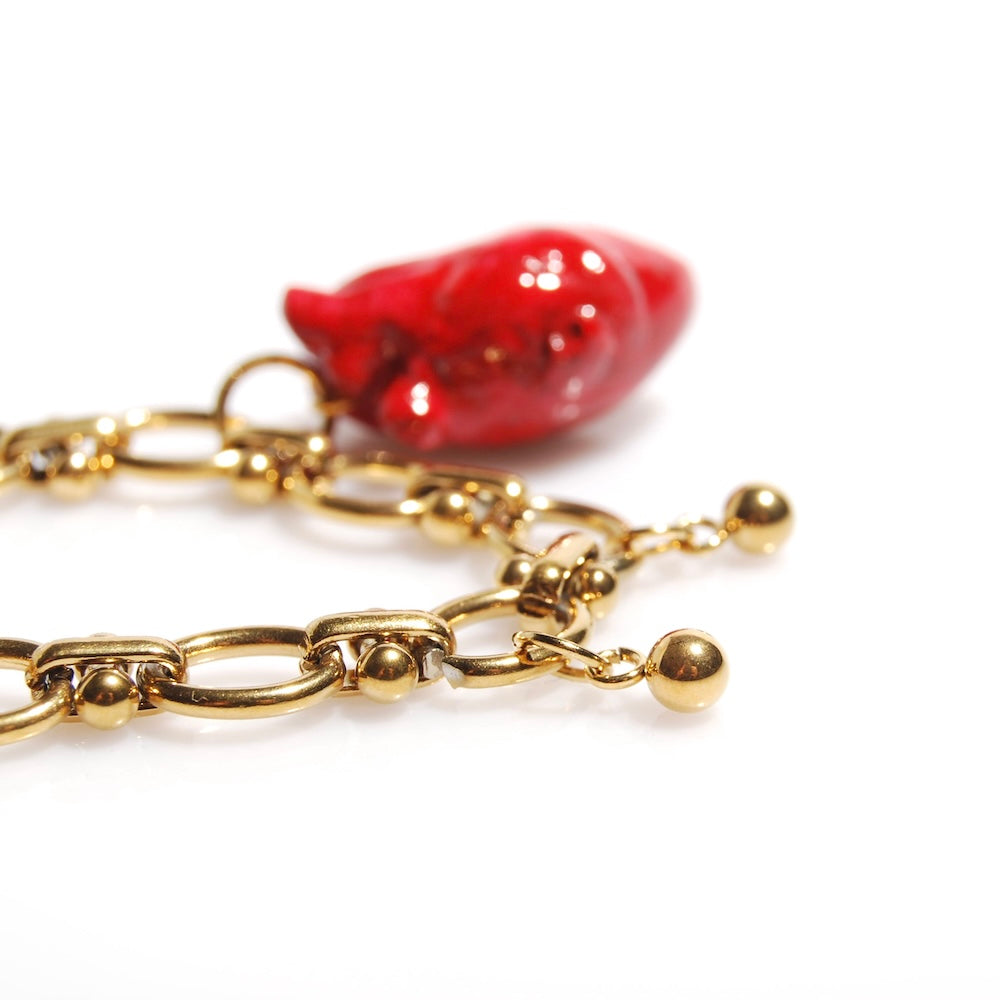 dettaglio di charms a sfera appesi ad un bracciale con catena spessa e pendente cuore anatomico rosso