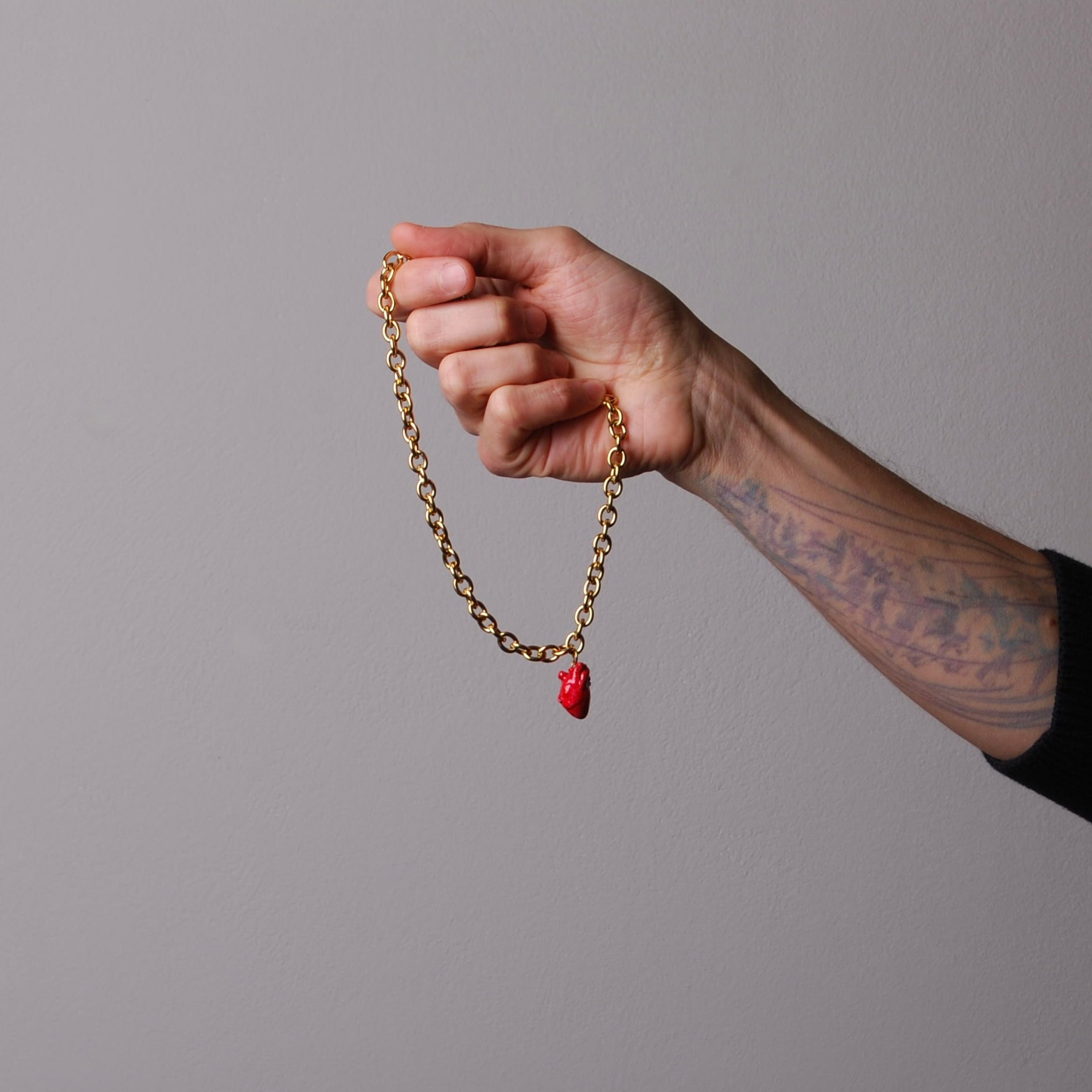 mano che impugna una collana a catena spessa con pendente cuore anatomico rosso