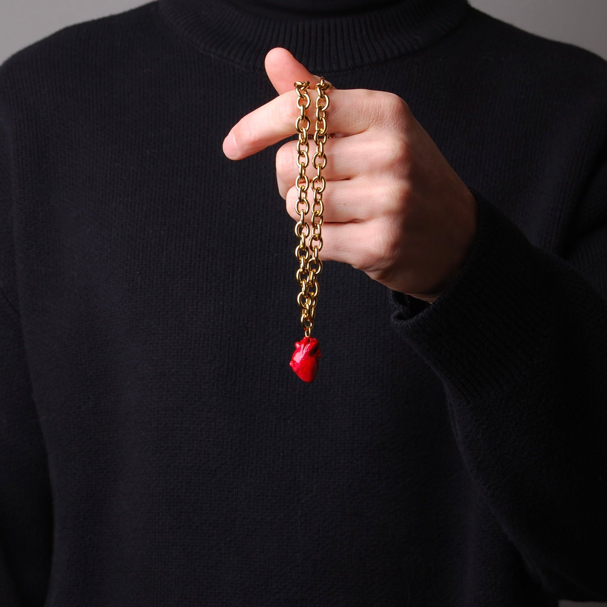 mano che tiene una collana a catena spessa con pendente cuore anatomico rosso