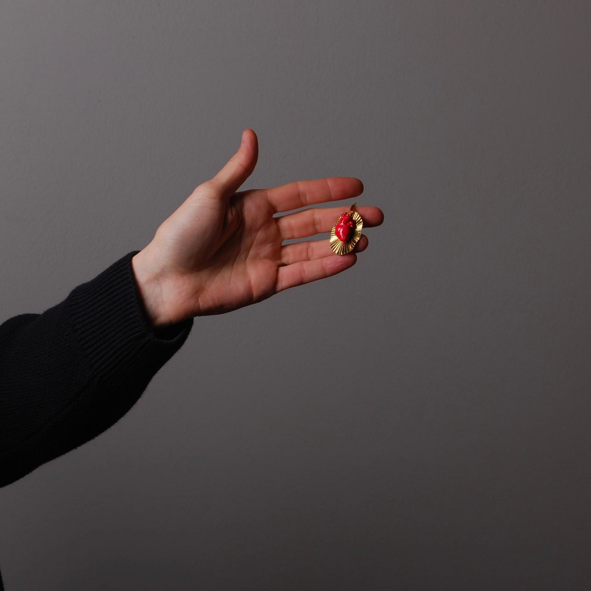 mano che sorregge un orecchini con cuore anatomico rosso su base plissettata
