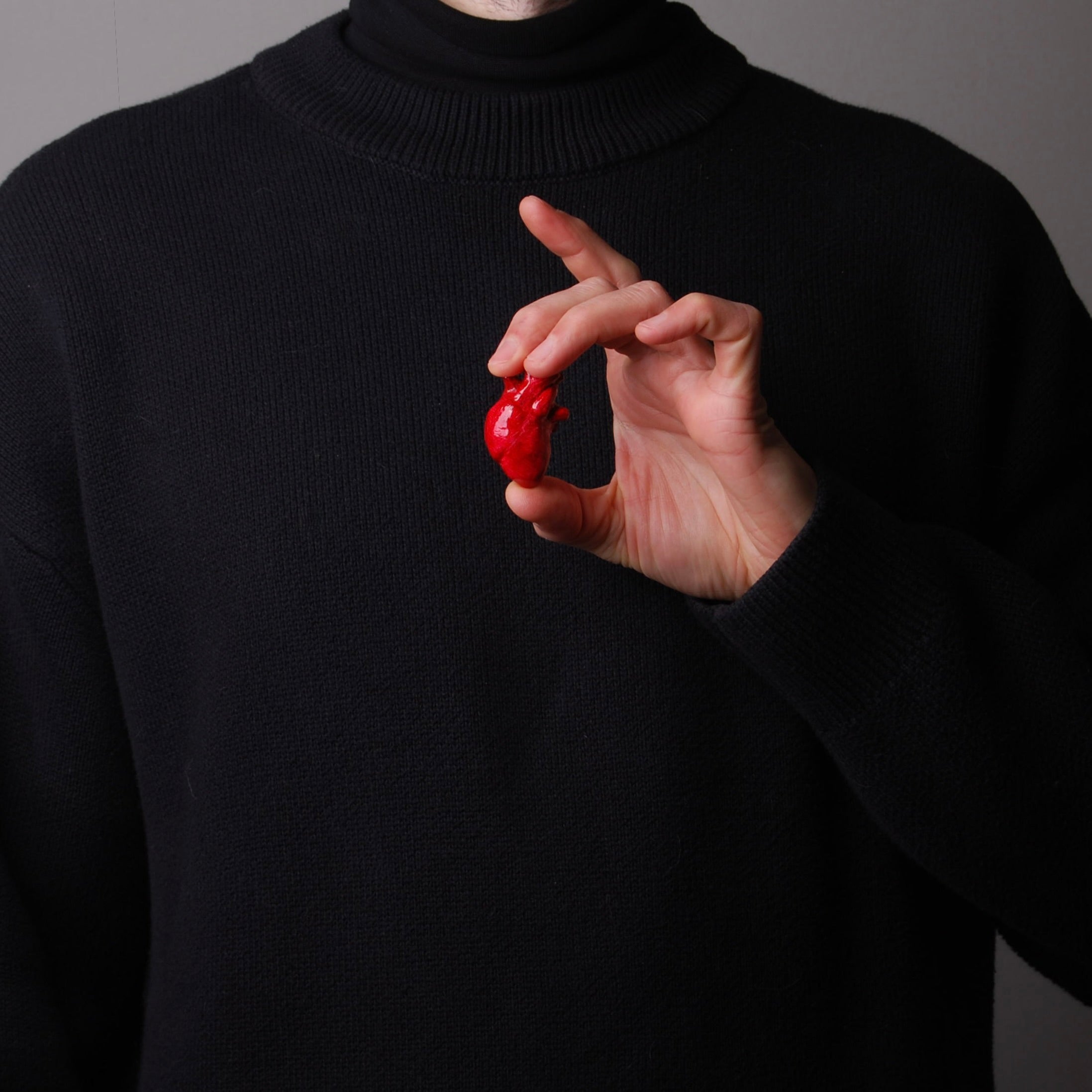 mano che sorregge una spilla cuore anatomico rosso