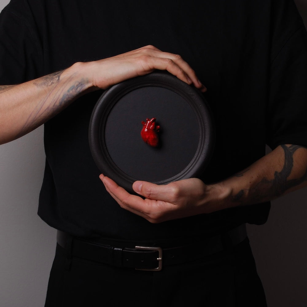 mani che tengono un quadretto rotondo con miniatura cuore anatomico rosso